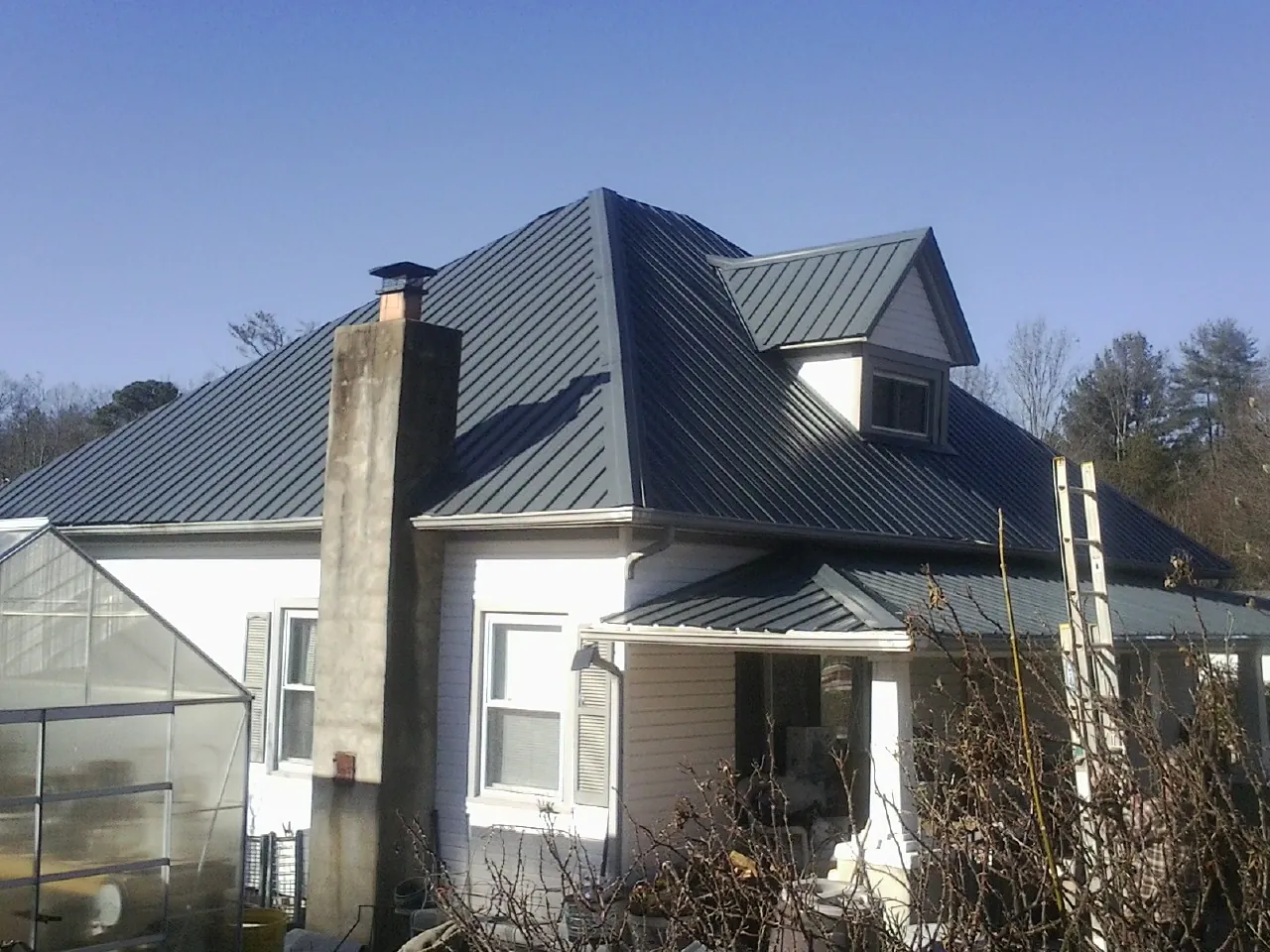Dark blue standing seam metal roof on a white farmhouse with dormer — Slate & Tile Roof Repair by Roofing Brothers in Newton Highlands