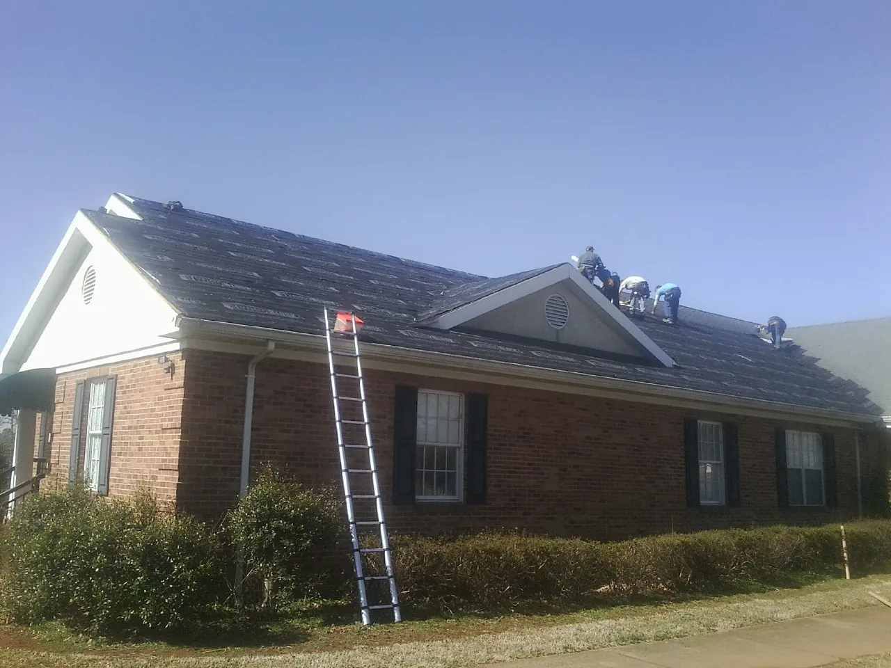 Crew tearing shingles off a brick ranch roof with a ladder set — Emergency Roof Repair work by our crew in Newton Highlands