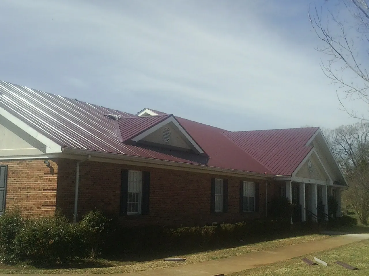 Red metal roof with gabled entries on a long brick building, from a Hail Damage Roof Repair job in Newton Highlands