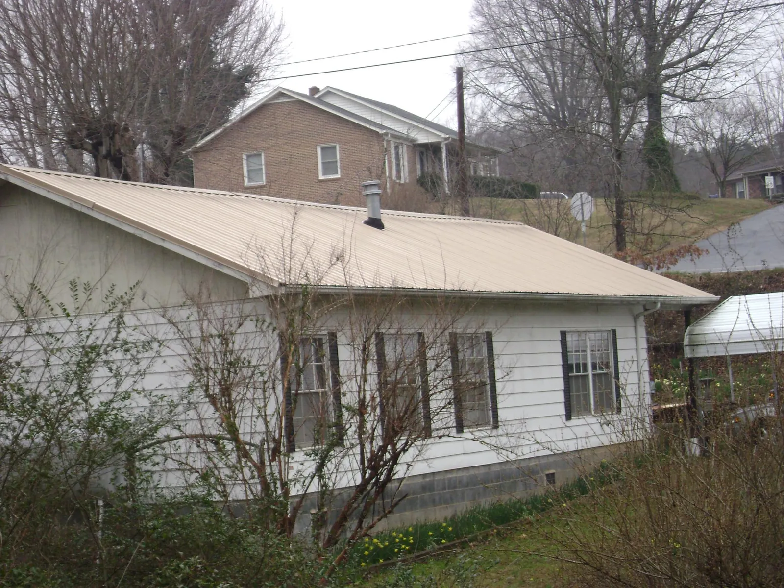 Tan metal roof on a white sided house set into a hillside — Commercial Roofing by Roofing Brothers in Newton Highlands