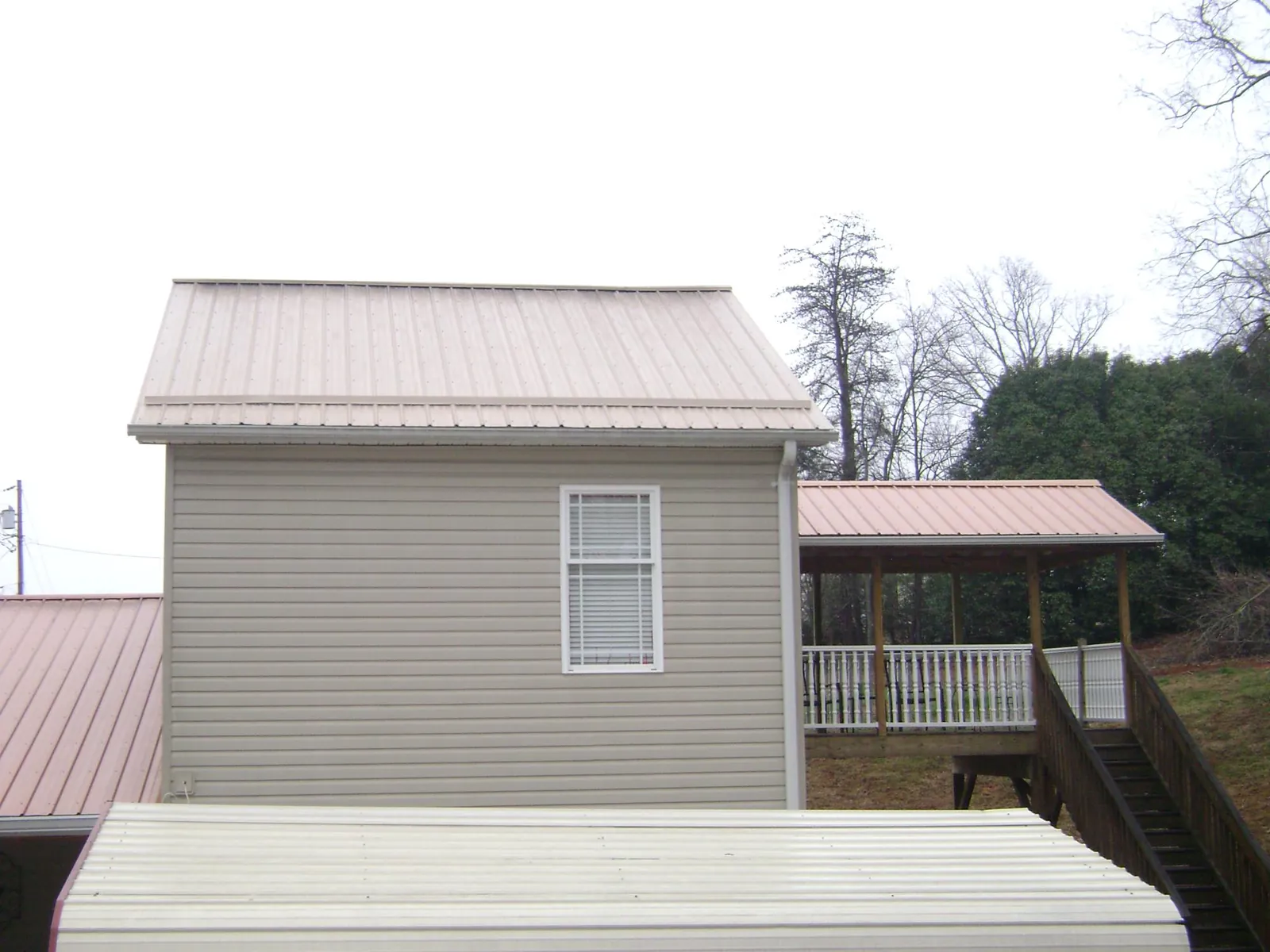 Tan metal roofs on a two story addition and attached porch, from a Roof Replacement job in Newton Highlands